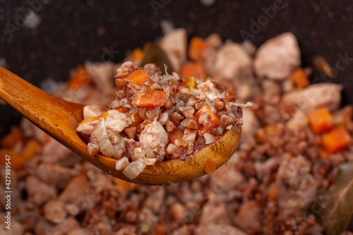 a lot of buckwheat with carrots and meat in a wooden spoon