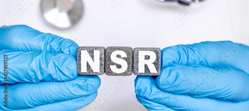 NSR Normal sinus rhythm of the heart - word from stone blocks with letters holding by a doctor's hands in medical protective gloves