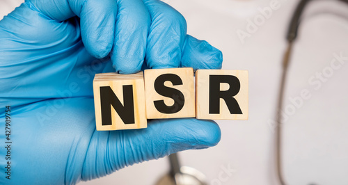 NSR Normal sinus rhythm of the heart - word from wooden blocks with letters holding by a doctor's hands in medical protective gloves. Medical concept. photo