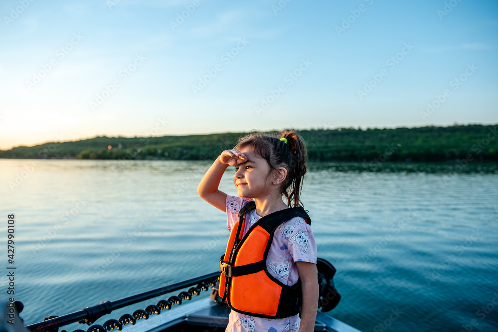 Little happy girl in a life jacket while walking on a boat 