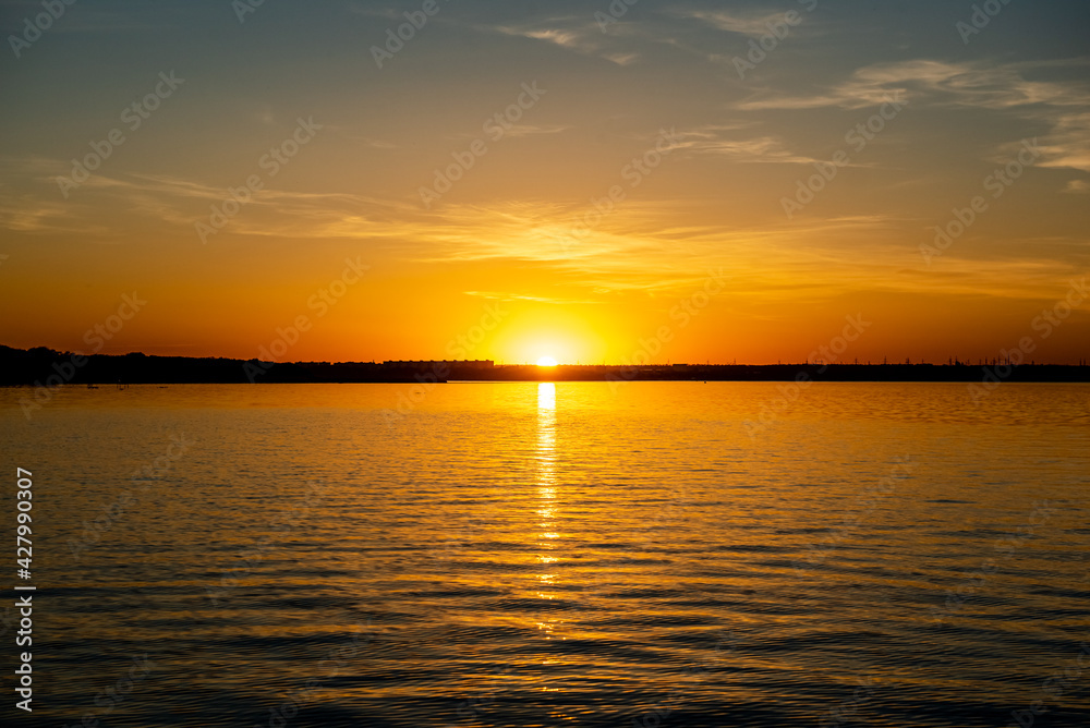 An early summer sunset over a lake in a small town in southern Russia, the sun is reflected in the water. 