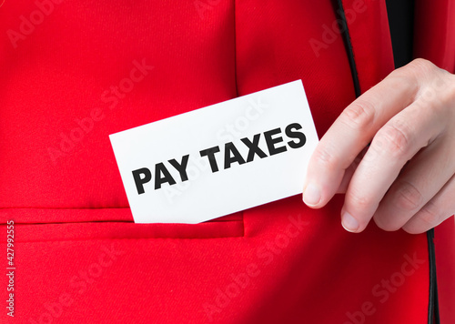 A businessman puts a white business card in his jacket pocket with the text PAY TAXES. Business concept.