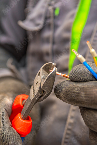 Electrician cuts electrical wires with pliers, installation of household electrical appliances, electrician tools. Vertical photo