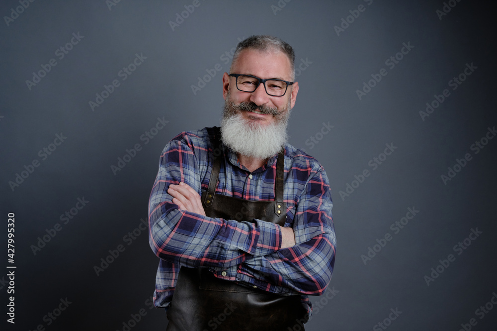 Portrait of handsome mature bearded man dressed leather apron isolated on gray background, caucasian workman with beard smiling Portrait of handsome mature bearded man dressed leather apron isolated on gray background, caucasian workman with beard smiling