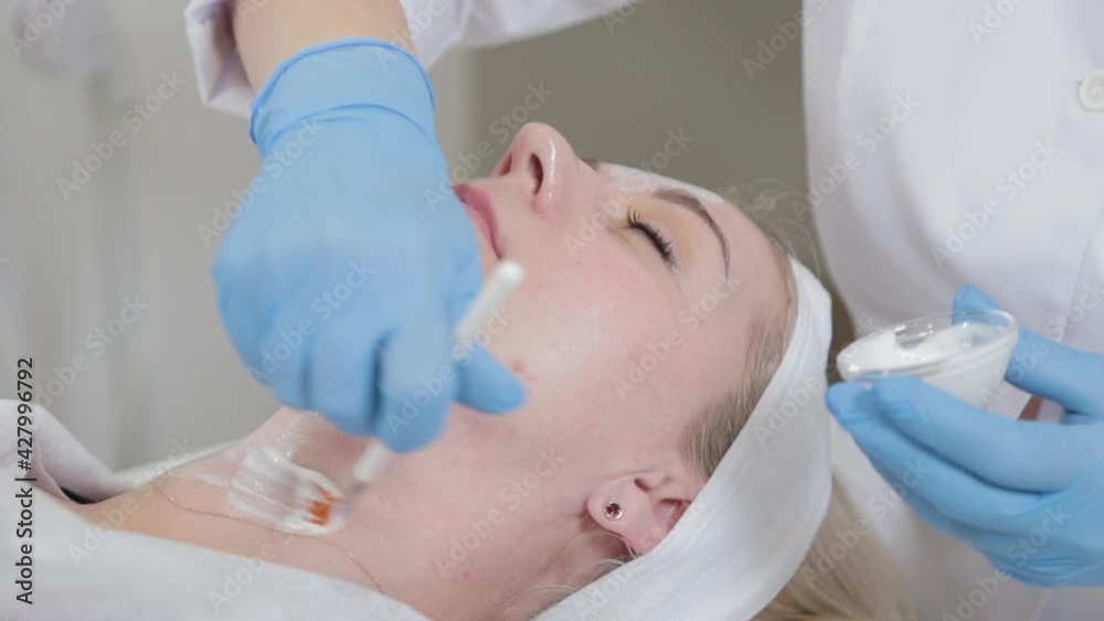 Professional beautician woman applies mask with brush on face. Professional beautician woman applies mask with brush on face.