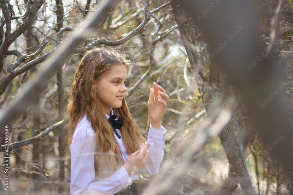 A girl stands with dried wildflowers, in the foreground and background blurred branches of bushes in the forest