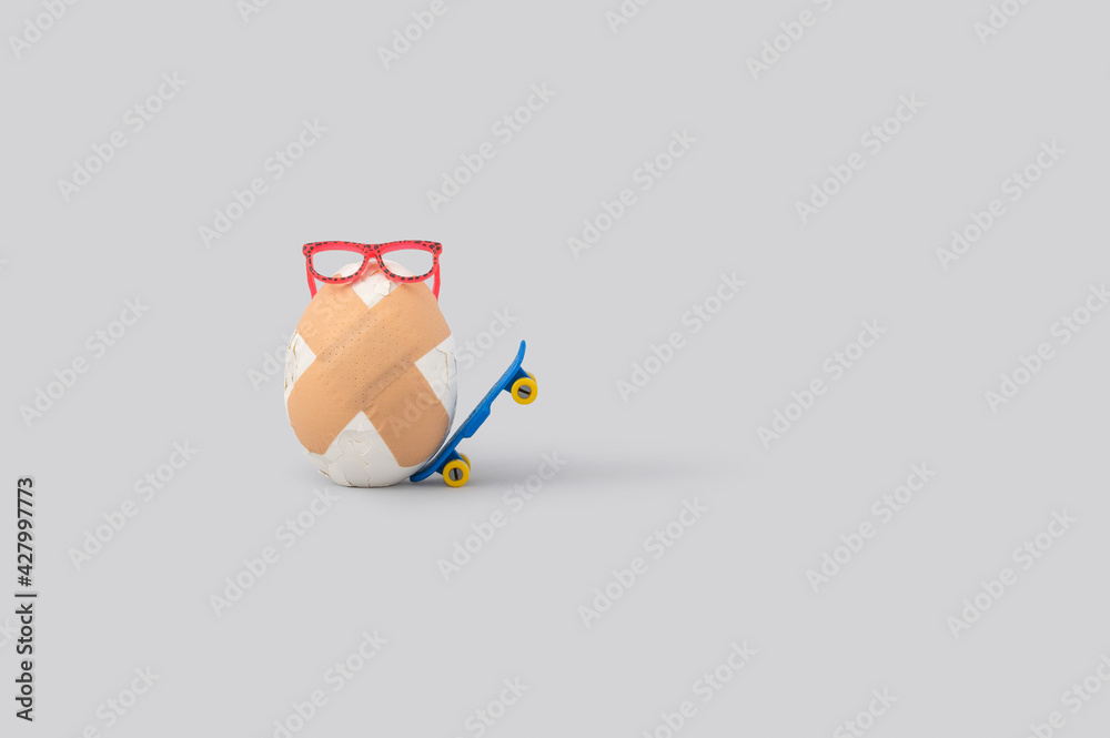Creative food layout with broken egg with adhesive bandage and skateboard on grey background