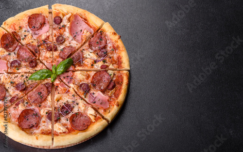 Delicious fresh oven pizza with tomatoes, salami and bacon on a dark concrete background