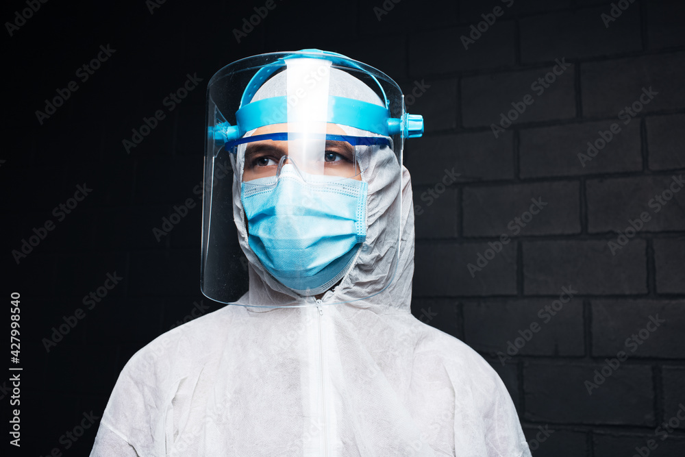 Studio dark portrait of young doctor man wearing PPE suit against coronavirus and covid-19. Background of black brick wall. Studio dark portrait of young doctor man wearing PPE suit against coronavirus and covid-19. Background of black brick wall.