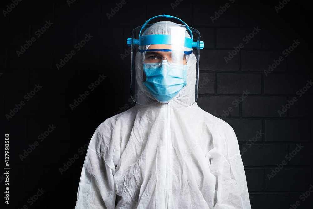 Studio dark portrait of young doctor man wearing PPE suit against coronavirus and covid-19. Background of black brick wall. Studio dark portrait of young doctor man wearing PPE suit against coronavirus and covid-19. Background of black brick wall.