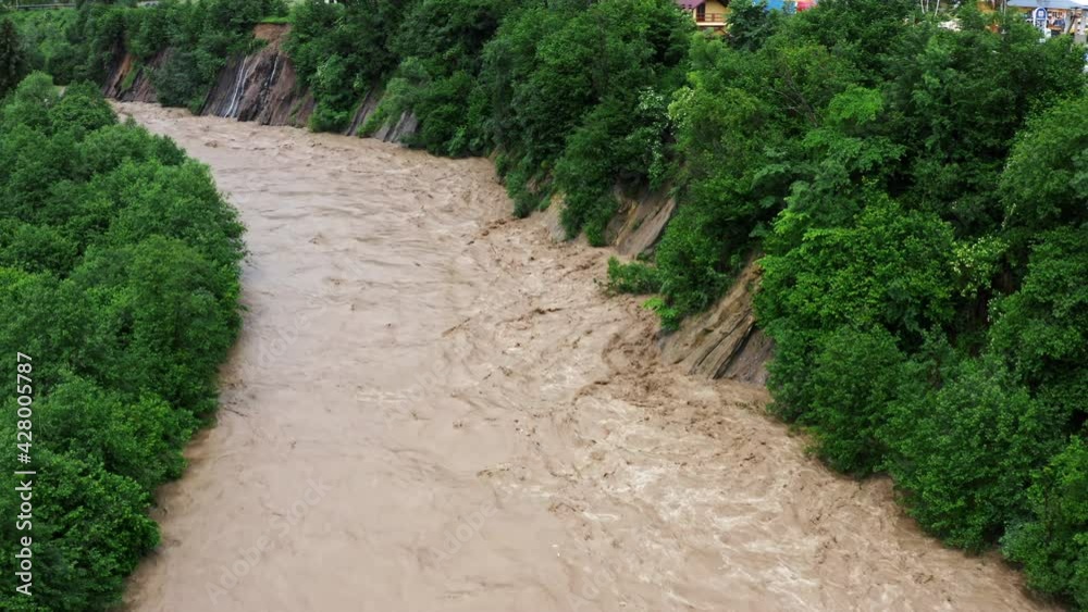 Fast flowing raging river after strong rain. Aerial flight above dirty mountain river roiling brown muddy water. Fast flowing raging river after strong rain. Aerial flight above dirty mountain river roiling brown muddy water.