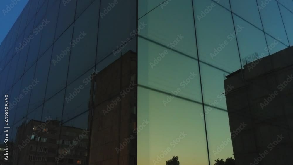 Outside view of business district building or mall with wall mirror windows at evening or night . Reflection of city , people , cars in mirrored walls . Drone camera moving . People working inside Outside view of business district building or mall with wall mirror windows at evening or night . Reflection of city , people , cars in mirrored walls . Drone camera moving . People working inside
