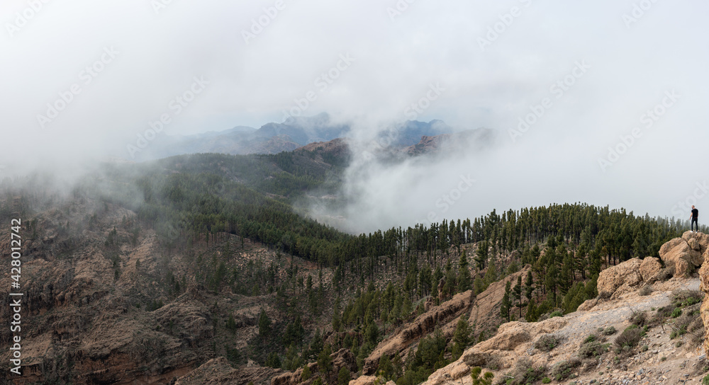 Mountain with low clouds and unrecognizable man watching from the side