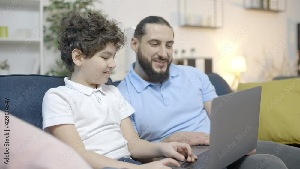 Dad and son making video call on laptop, smiling and talking, modern technology Dad and son making video call on laptop, smiling and talking, modern technology