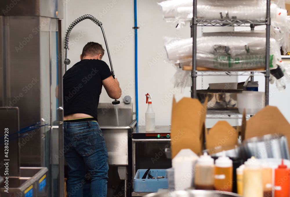 Restaurant employee washing dishes in an industrial kitchen sink Stock