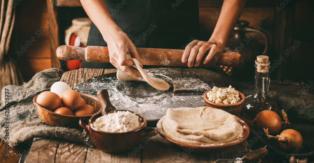 Woman hands rolls the dough with a rolling pin on rustic wooden background. Cooking bread with cheese, eggs and herb. Homemade healthy food concept, toning Woman hands rolls the dough with a rolling pin on rustic wooden background. Cooking bread with cheese, eggs and herb. Homemade healthy food concept, toning