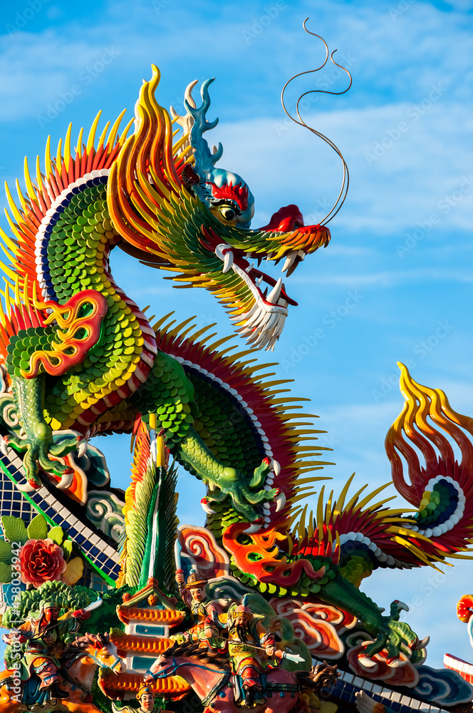 Incredible statue of super colorful dragon, seated, looking back, with long ears and mustaches being illuminated by the sun, contrasting its vibrant colors with the blue of the sky. Incredible statue of super colorful dragon, seated, looking back, with long ears and mustaches being illuminated by the sun, contrasting its vibrant colors with the blue of the sky.