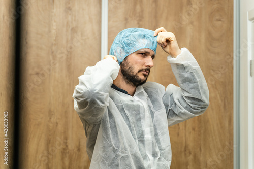 Portrait of caucasian man wearing protective mask and bouffant mob cap - Young male doctor or scientist getting ready for work in the laboratory hospital front view copy space