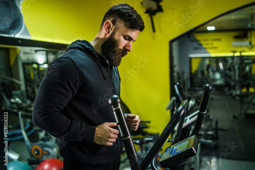 Adult caucasian male athlete training on the treadmill at the gym - back view of man with beard in black hoodie running on the treadmill sport and fitness concept back view copy space