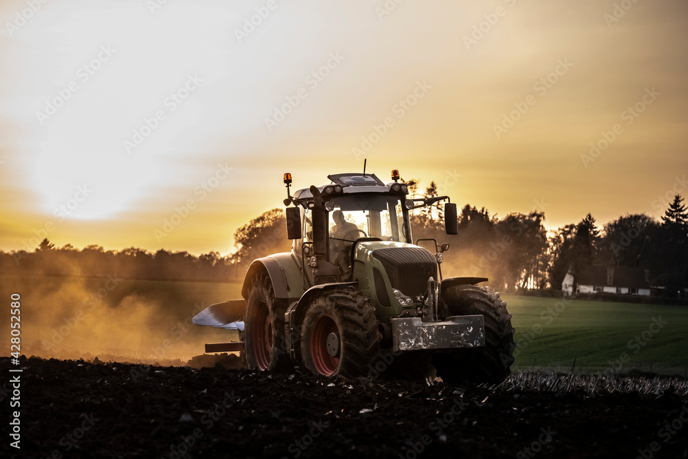 Ploughing a field at sunset with a tractor and plough, ready for crops on a farm Ploughing a field at sunset with a tractor and plough, ready for crops on a farm
