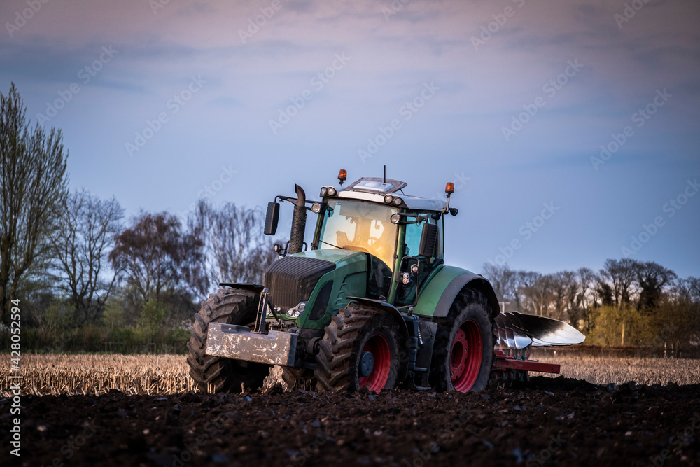Ploughing a field at sunset with a tractor and plough, ready for crops on a farm Ploughing a field at sunset with a tractor and plough, ready for crops on a farm