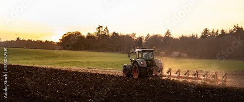 Ploughing a field at sunset with a tractor and plough, ready for crops on a farm photo