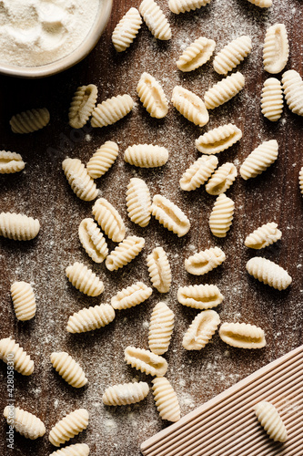 Homemade cavatelli pasta on a cutting board next to a small bowl of flour and a gnocchi board. photo