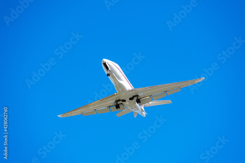 Small business jet with landing lights and deployed landing gear preparing for landing at airport.
