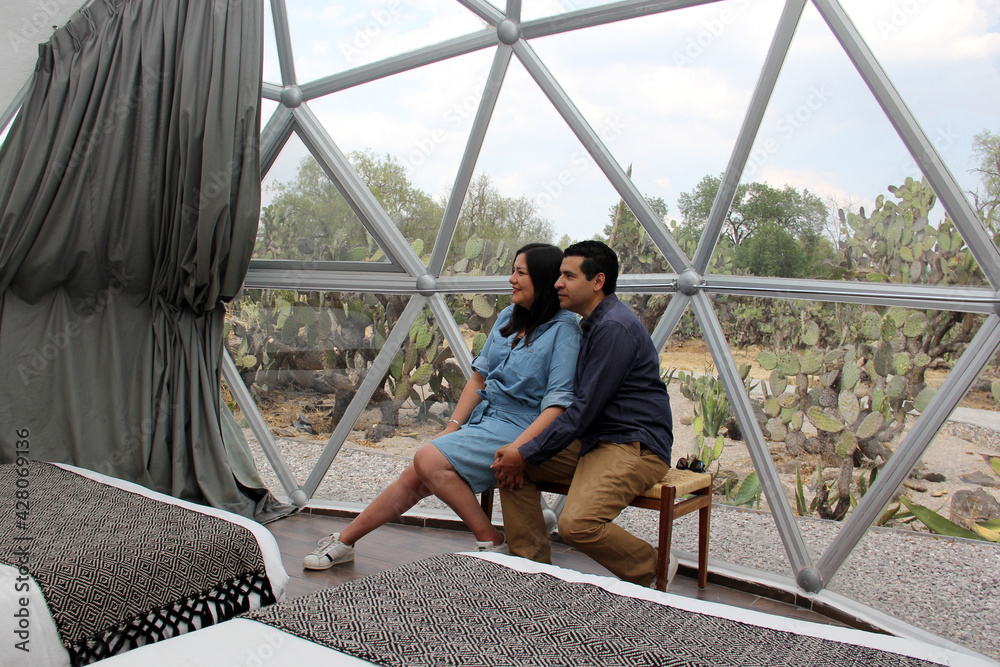 Latin couple in love inside glamping dome room with desert vegetation outside