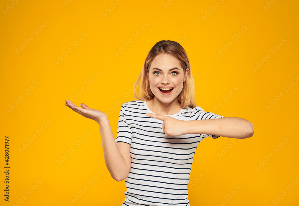 Pretty blonde on a yellow background shows her hand towards emotions positive gesture smile model Pretty blonde on a yellow background shows her hand towards emotions positive gesture smile model