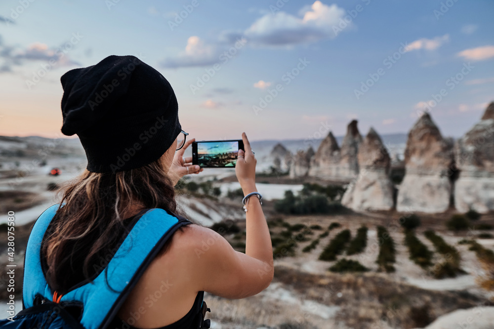 Beautiful tourist woman taking picture of Stone houses on her smartphone in Love valley in Goreme village.