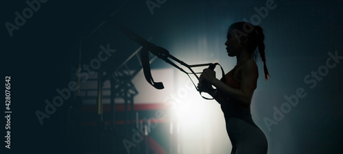 Silhouette of young Sexy fit Asian woman using TRX exercise equipment at the gym. Young strong lady with healthy lifestyle workout motivation