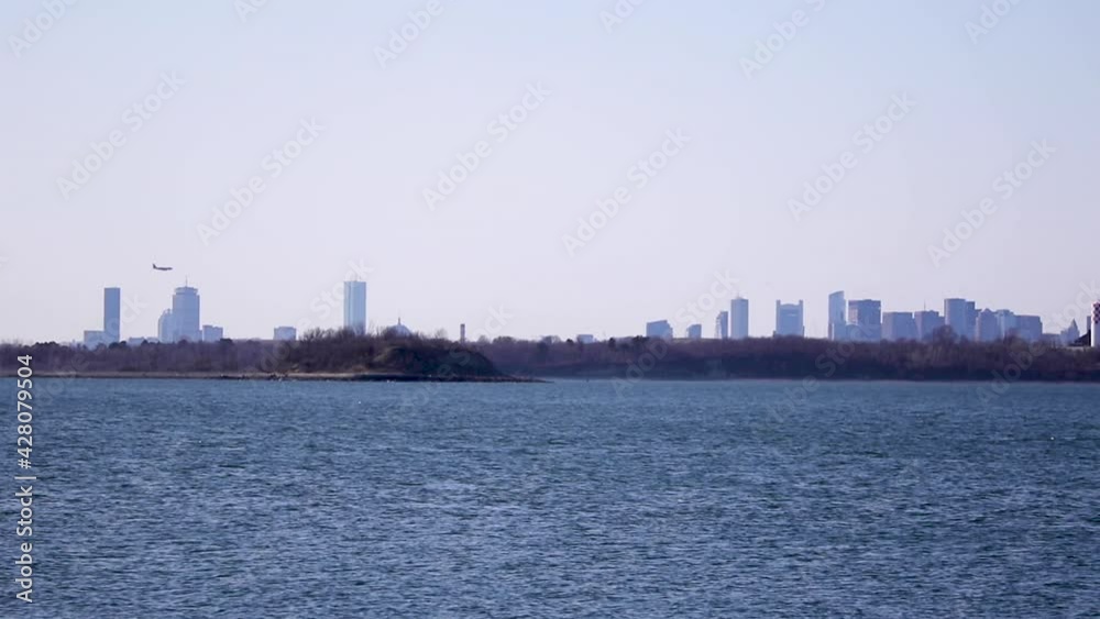 Distant view of Boston Skyline, aircraft coming into frame from left to land at Boston International Airport. Static Distant view of Boston Skyline, aircraft coming into frame from left to land at Boston International Airport. Static