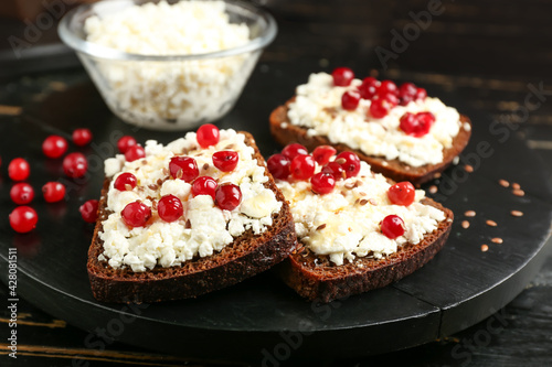 Bread with cottage cheese and red currants on dark wooden background