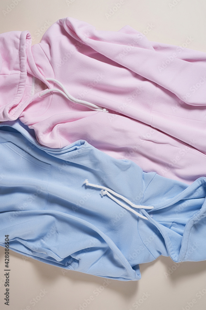 Flat lay of two blue and pink pastel blank cotton hoodie isolated over pale beige background