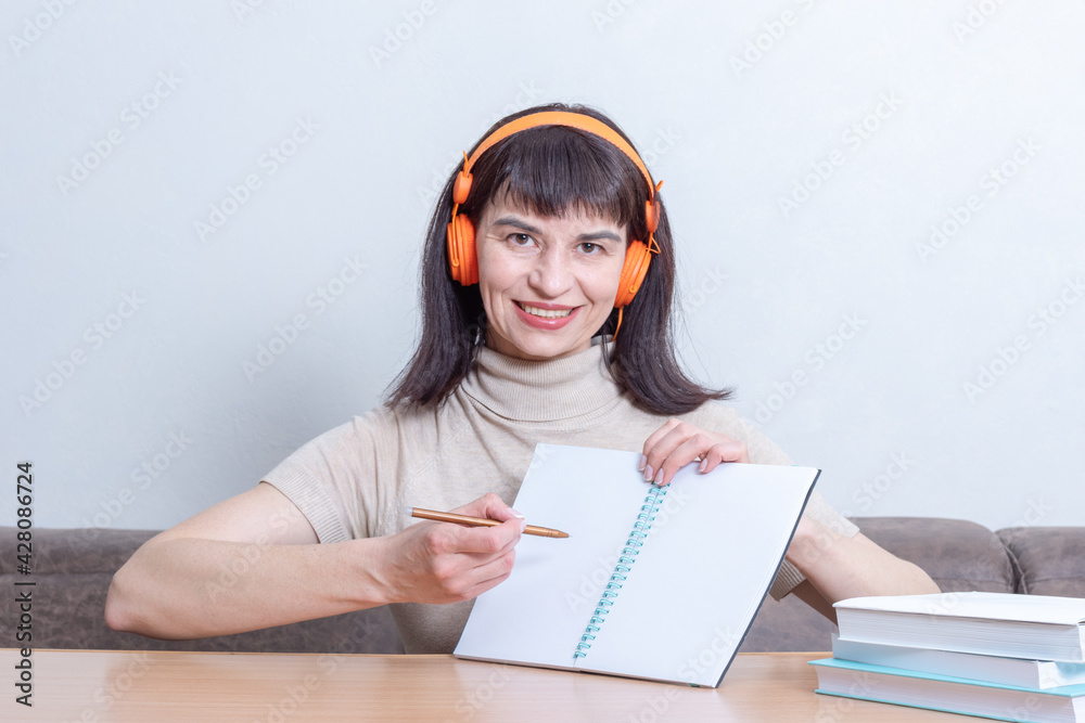 Smiling woman teacher in headphones explains the lesson by showing on a blank exercise book. Back to school Smiling woman teacher in headphones explains the lesson by showing on a blank exercise book. Back to school