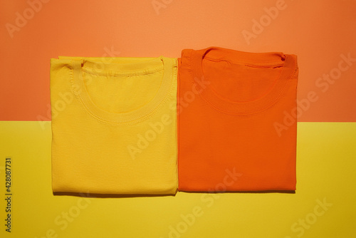 Two folded yellow and orange cotton t shirts isolated on creative colorful background. Flat lay tees template