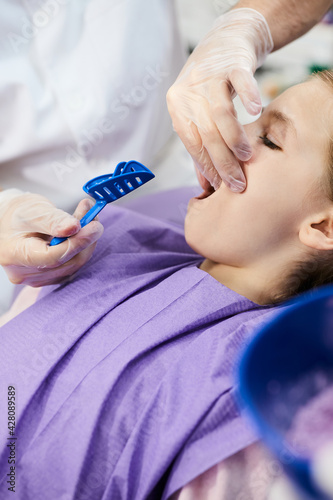 Close-up of orthodontist taking dental impression of small girl's teeth at dentist's office.