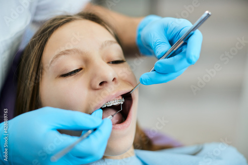 Little girl having her braces checked by orthodontist at dentist s office.