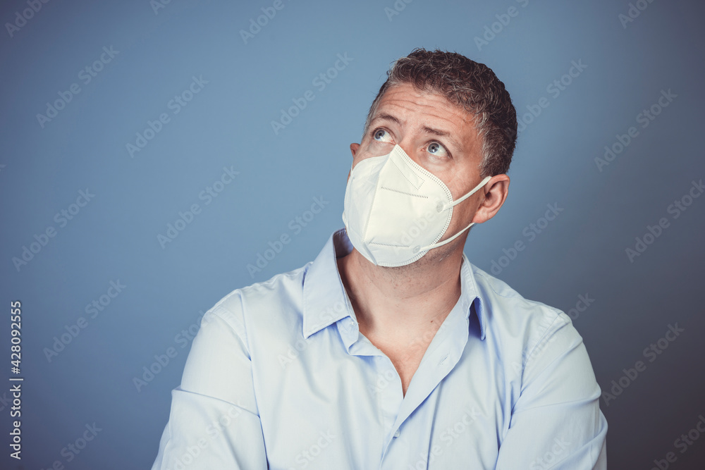 Middle-aged man with ffp2 protective mask and blue shirt in front of blue background during lockdown Middle-aged man with ffp2 protective mask and blue shirt in front of blue background during lockdown