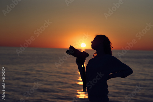 silhouette of a woman with a camera at sunset near the sea beach landscape
