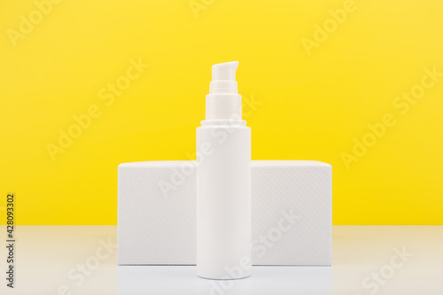 Face moisturizing cream or lotion in tall white tube against white geometric podium and yellow background with copy space. Concept of skin moisturizing and protective treatment with Spf for summer