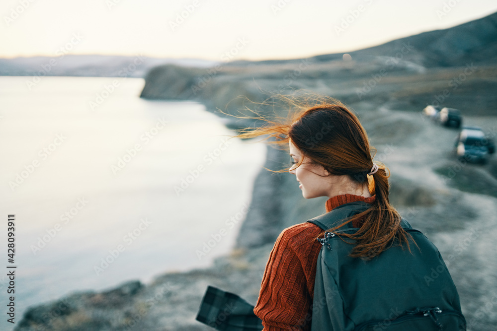 portrait of woman with backpack on nature in the mountains near the sea at sunset cropped view
