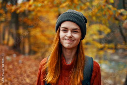 portrait of a beautiful woman in a hat sweater with a backpack on her back in the autumn forest in nature