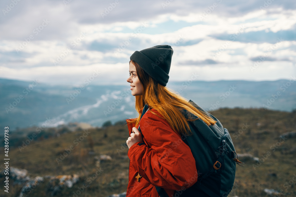 woman travels in the mountains landscape backpack red jacket and hat model