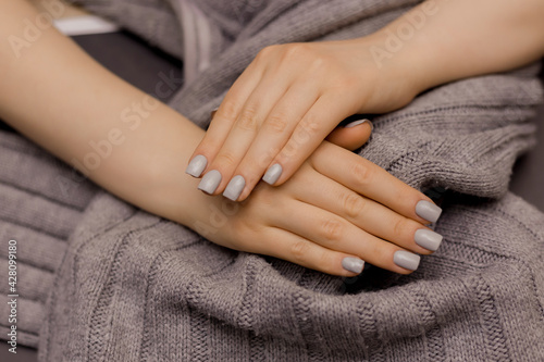 Nail Polish. Art Manicure. Modern style gray Nail Polish.Stylish pastel gray color. Nails holding knitted wool material Shellac. Copy space.Female hand with graynail design. Woman hand on gray fabric 