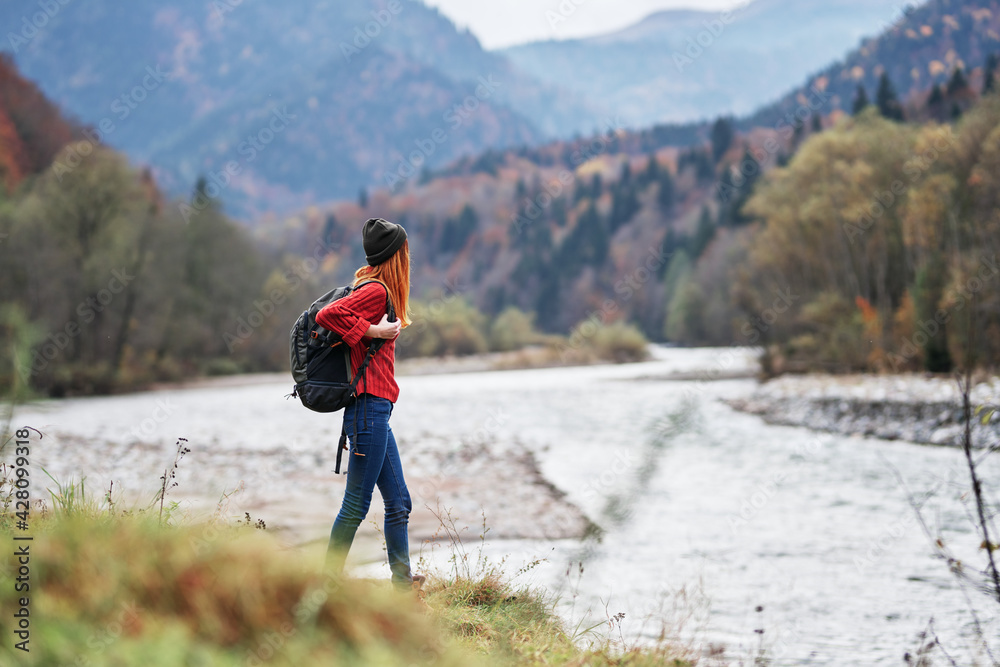 woman in a red sweater with a backpack in the mountains on nature near the river pond lake