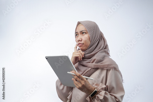 portrait of a young woman with hijab thinking and holding a tablet computer isolated in white