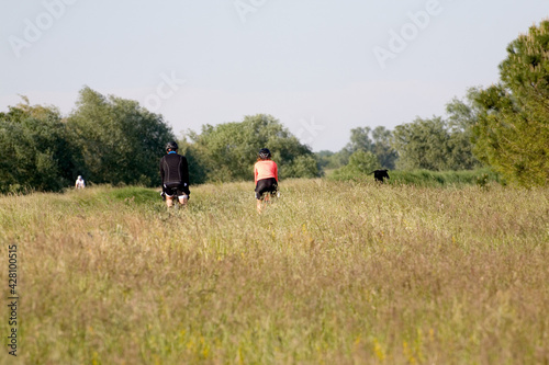 Two cyclists travel along a road that is not visible because it is surrounded by tall grass in a wild landscape