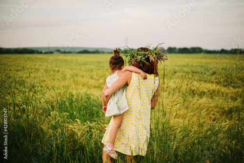 mom and daughter playing in the field. women have a wreath of wildflowers on their heads.
